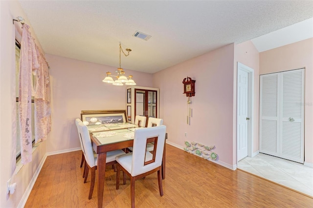 dining area featuring a textured ceiling, light hardwood / wood-style flooring, and an inviting chandelier