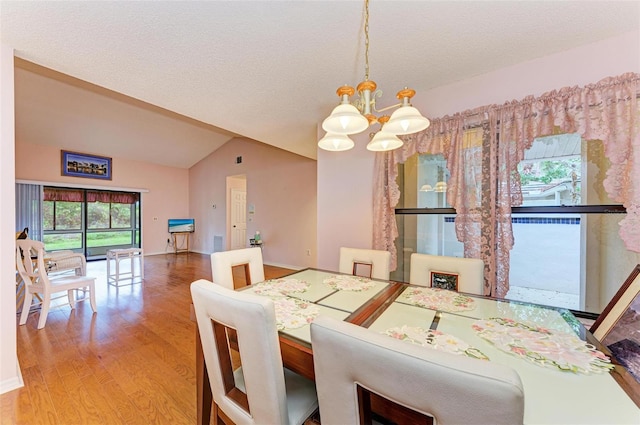 dining space with a textured ceiling, hardwood / wood-style floors, vaulted ceiling, and an inviting chandelier