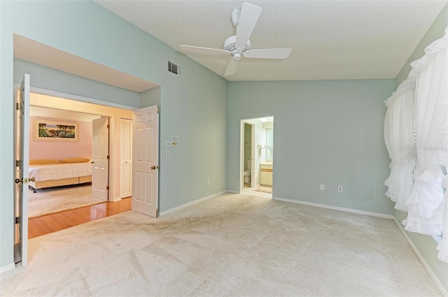 unfurnished bedroom featuring connected bathroom, ceiling fan, light colored carpet, a textured ceiling, and vaulted ceiling