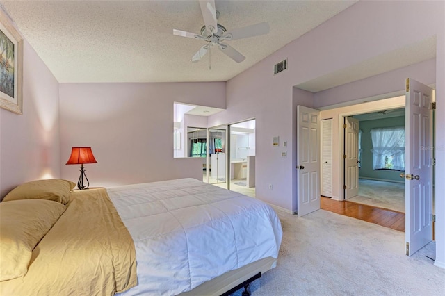 bedroom with light carpet, ensuite bath, vaulted ceiling, ceiling fan, and a textured ceiling