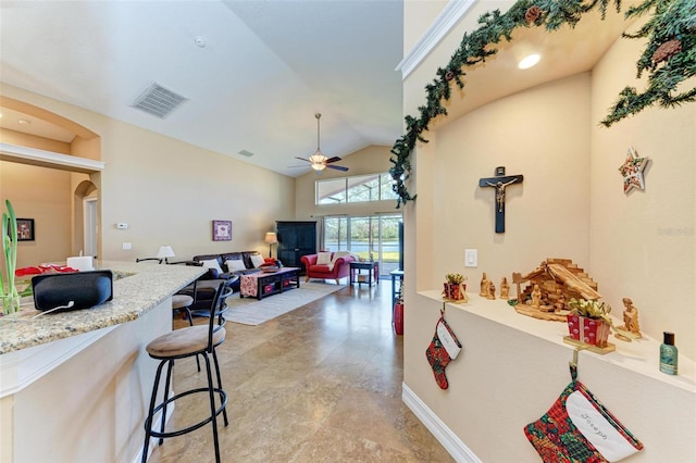 kitchen featuring ceiling fan, a breakfast bar, vaulted ceiling, and light stone counters