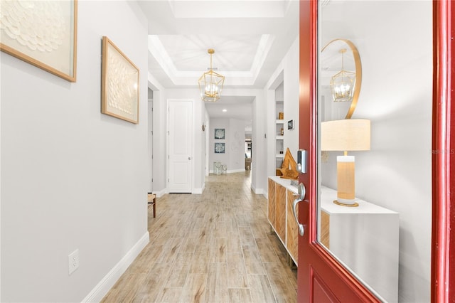 hallway featuring an inviting chandelier, a tray ceiling, and light hardwood / wood-style flooring