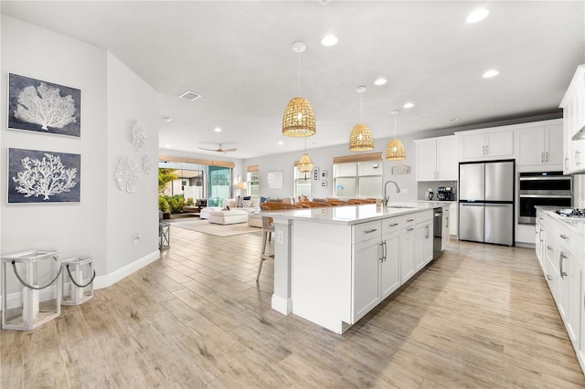 kitchen featuring white cabinetry, a kitchen island with sink, decorative light fixtures, and appliances with stainless steel finishes