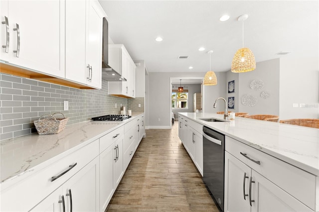 kitchen with white cabinets, wall chimney range hood, sink, decorative light fixtures, and stainless steel appliances