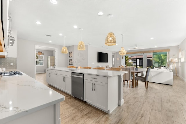 kitchen with backsplash, a center island with sink, hanging light fixtures, white cabinetry, and stainless steel appliances