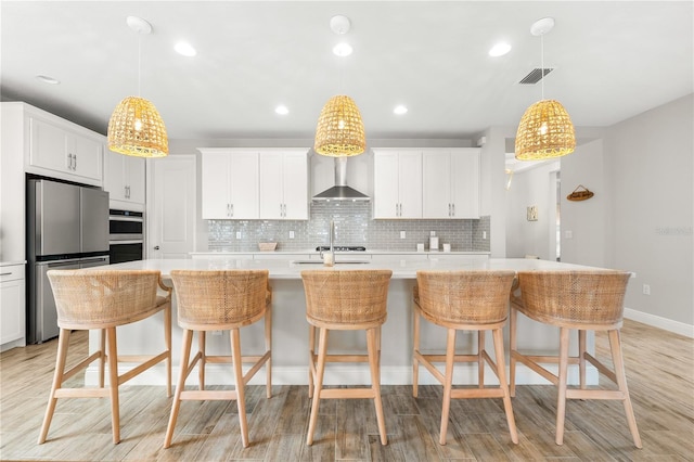 kitchen featuring white cabinets, a kitchen island with sink, wall chimney exhaust hood, and stainless steel appliances