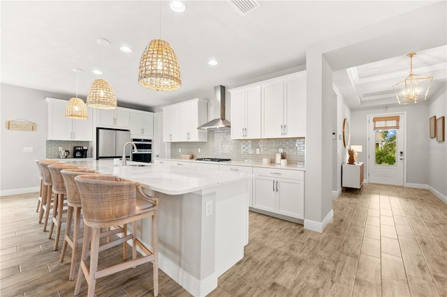 kitchen featuring stainless steel fridge, a spacious island, wall chimney range hood, pendant lighting, and white cabinetry