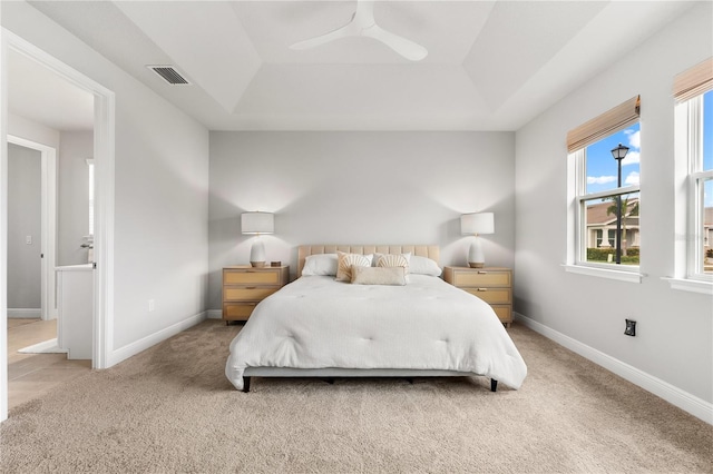 bedroom featuring light colored carpet, a raised ceiling, and ceiling fan