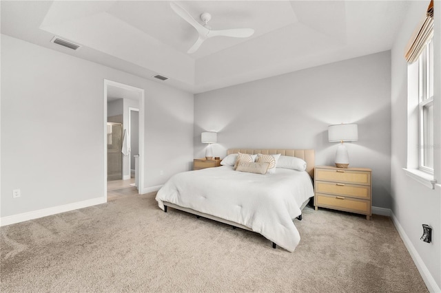 bedroom featuring ceiling fan, light colored carpet, multiple windows, and a tray ceiling