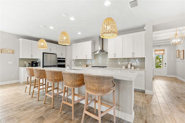 kitchen with a center island with sink, white cabinetry, wall chimney range hood, and stainless steel appliances