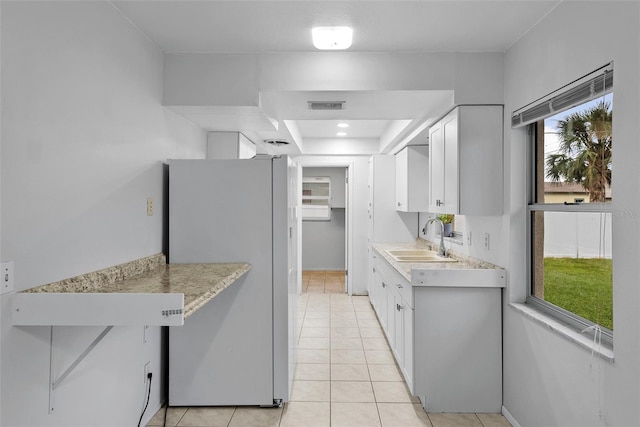 kitchen with stainless steel refrigerator, light tile patterned floors, plenty of natural light, sink, and white cabinetry