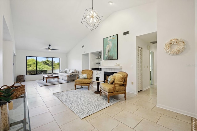 tiled living room with ceiling fan with notable chandelier, high vaulted ceiling, and a tiled fireplace