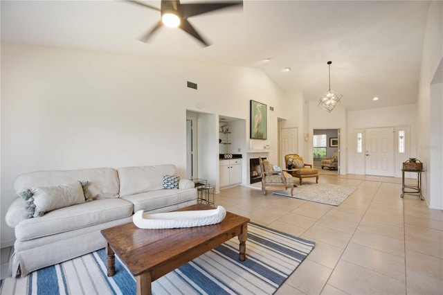 living room with ceiling fan with notable chandelier, a fireplace, high vaulted ceiling, and light tile patterned floors