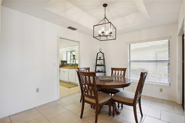 dining space with light tile patterned floors, a notable chandelier, sink, and a tray ceiling