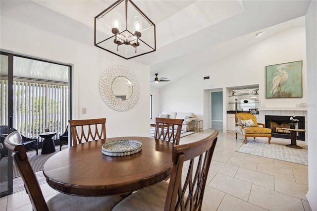 dining area with a tile fireplace, light tile patterned floors, built in features, lofted ceiling, and ceiling fan with notable chandelier