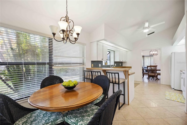 dining room with ceiling fan with notable chandelier, vaulted ceiling, light tile patterned floors, and a wealth of natural light