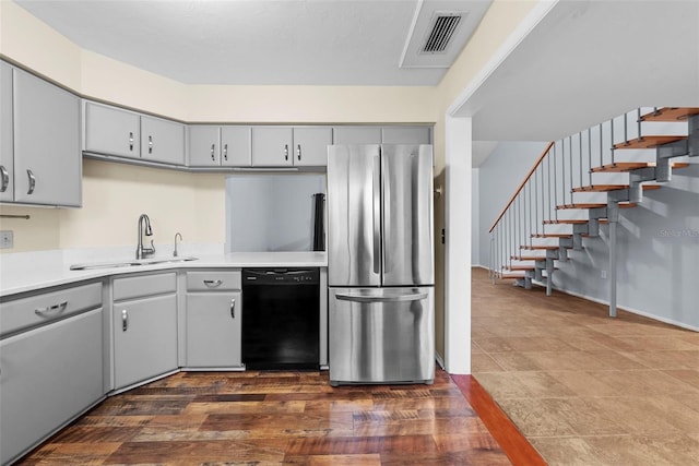 kitchen with sink, dark hardwood / wood-style floors, gray cabinets, black dishwasher, and stainless steel refrigerator