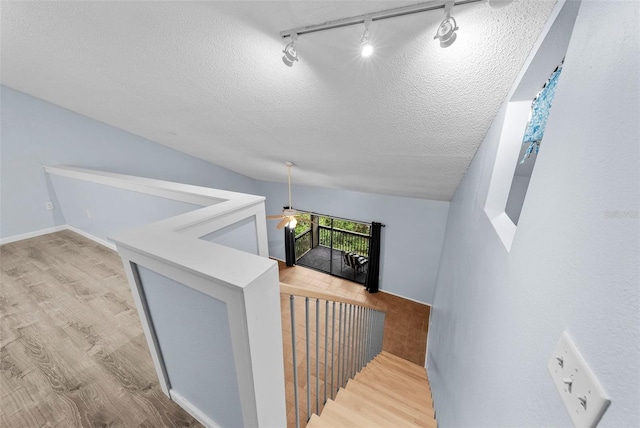 stairway featuring ceiling fan, a textured ceiling, vaulted ceiling, track lighting, and hardwood / wood-style flooring