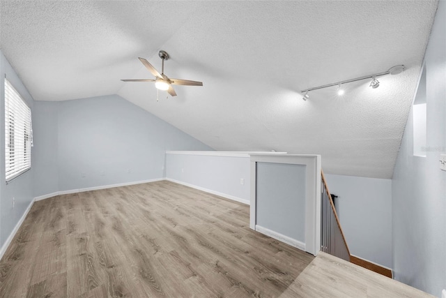 additional living space featuring a textured ceiling, ceiling fan, light hardwood / wood-style floors, and vaulted ceiling