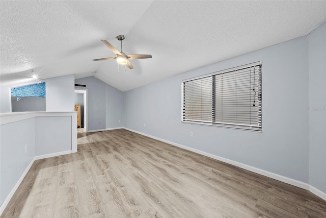 empty room featuring ceiling fan, light wood-type flooring, a textured ceiling, and vaulted ceiling