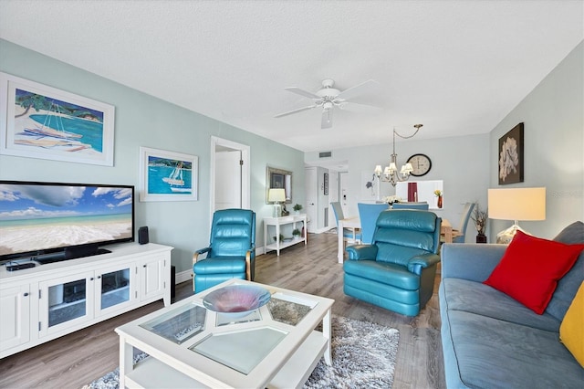 living room featuring ceiling fan with notable chandelier, wood-type flooring, and a textured ceiling