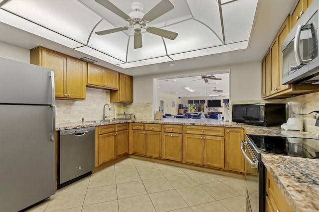 kitchen with light stone countertops, appliances with stainless steel finishes, backsplash, sink, and light tile patterned floors