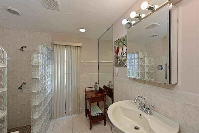 bathroom featuring tiled shower, tile patterned floors, tile walls, a textured ceiling, and sink