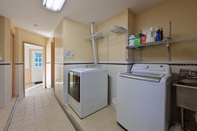 clothes washing area featuring sink, washer and clothes dryer, tile walls, and light tile patterned floors