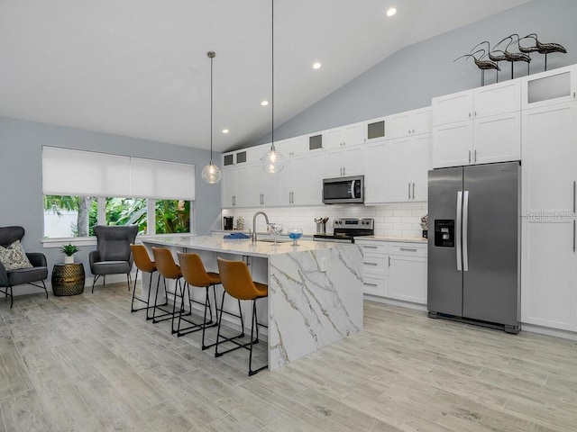 kitchen with glass insert cabinets, light stone countertops, a kitchen island with sink, stainless steel appliances, and white cabinetry