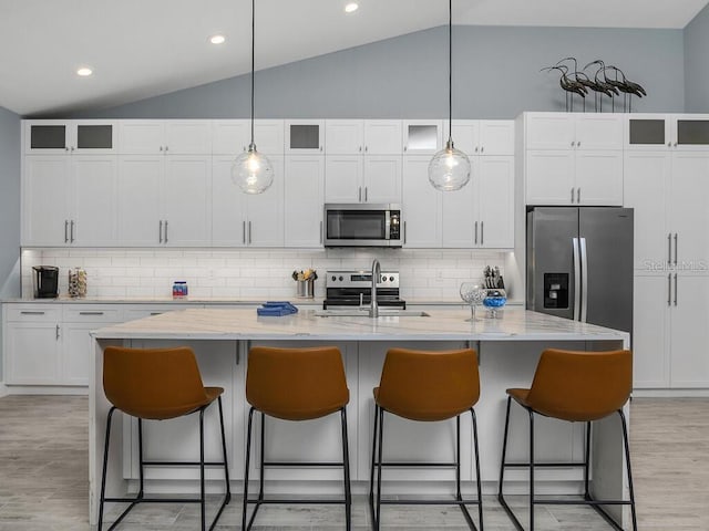 kitchen with a kitchen island with sink, stainless steel appliances, glass insert cabinets, and pendant lighting