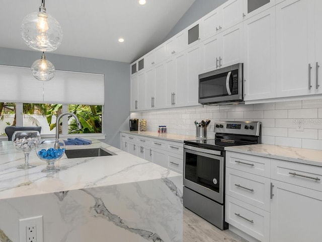 kitchen featuring stainless steel appliances, a sink, white cabinetry, hanging light fixtures, and glass insert cabinets