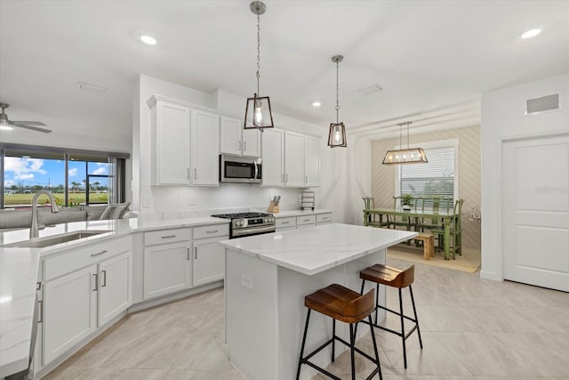 kitchen with pendant lighting, white cabinets, ceiling fan, appliances with stainless steel finishes, and light stone counters