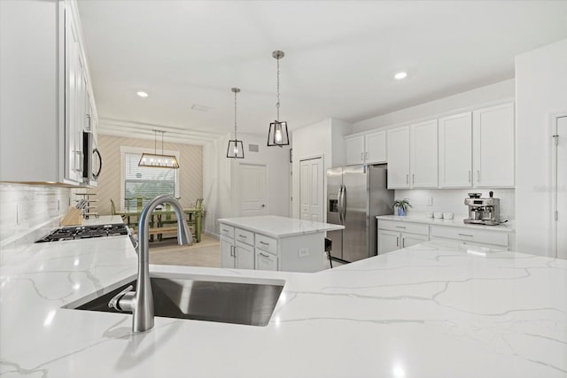 kitchen featuring stainless steel fridge, sink, white cabinets, a center island, and hanging light fixtures