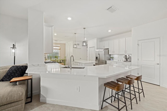 kitchen featuring sink, stainless steel fridge, white cabinetry, a kitchen bar, and kitchen peninsula