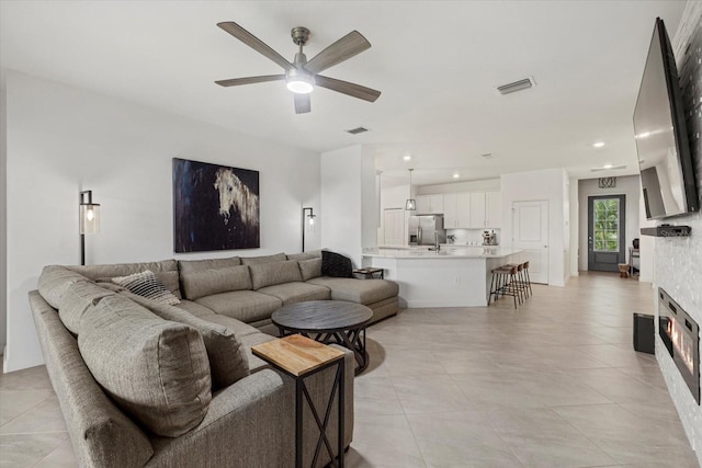 living room with a stone fireplace and ceiling fan