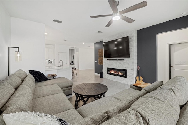 living room featuring ceiling fan, a stone fireplace, and sink