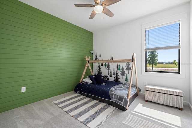 carpeted bedroom featuring ceiling fan and wooden walls