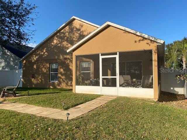 back of property with a sunroom and a lawn