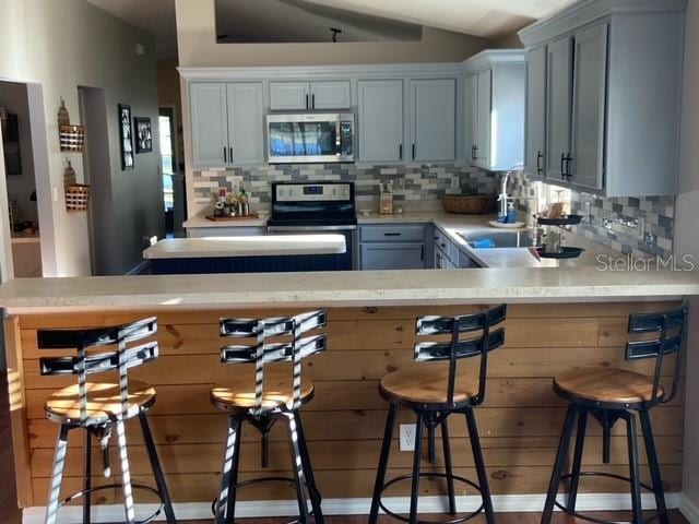 kitchen with stainless steel appliances, gray cabinetry, backsplash, and a kitchen bar