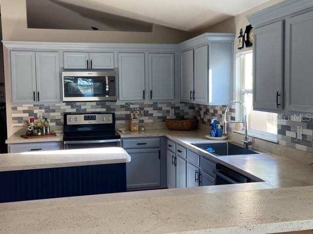 kitchen featuring lofted ceiling, sink, gray cabinets, appliances with stainless steel finishes, and backsplash