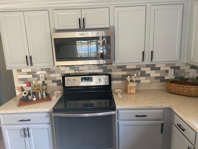 kitchen with tasteful backsplash, light stone countertops, stainless steel appliances, and white cabinets