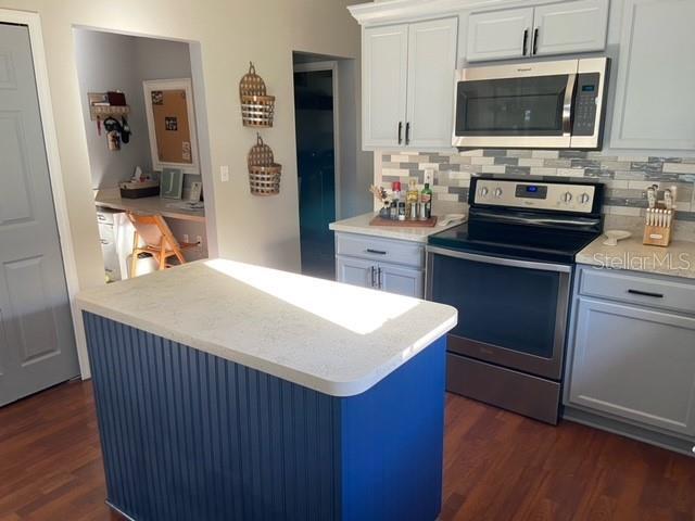 kitchen featuring appliances with stainless steel finishes, tasteful backsplash, white cabinets, a kitchen island, and dark hardwood / wood-style flooring