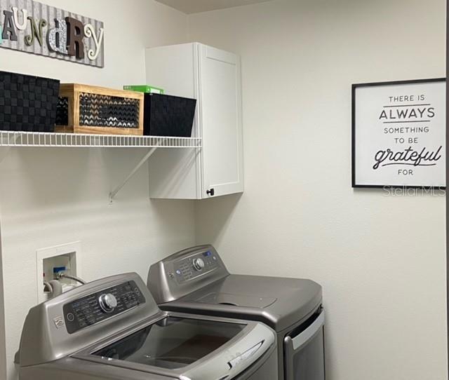 clothes washing area with separate washer and dryer and cabinets