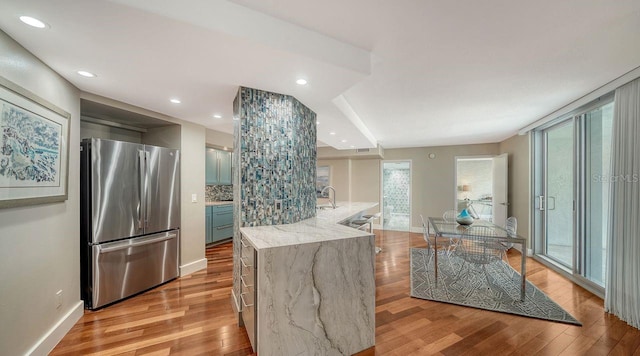 kitchen with stainless steel refrigerator, tasteful backsplash, a kitchen island with sink, light hardwood / wood-style floors, and light stone countertops