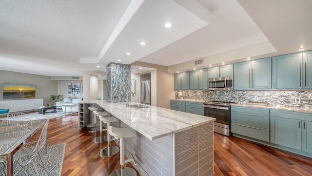 kitchen featuring a large island, sink, stainless steel appliances, light stone countertops, and decorative backsplash