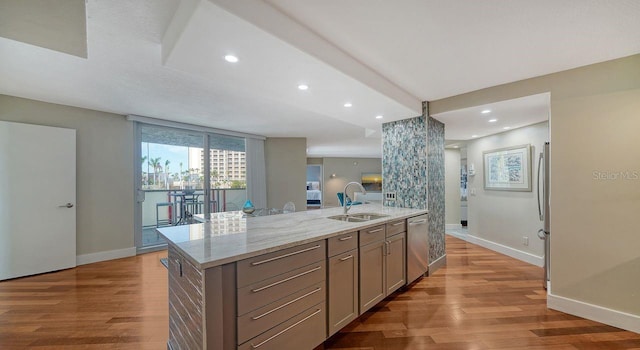 kitchen with sink, light stone counters, a center island with sink, light hardwood / wood-style flooring, and appliances with stainless steel finishes