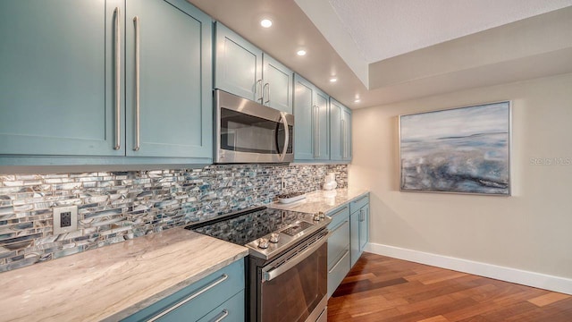 kitchen with stainless steel appliances, dark hardwood / wood-style flooring, blue cabinets, and backsplash