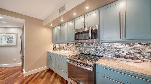 kitchen with stainless steel appliances, hardwood / wood-style floors, light stone counters, and decorative backsplash