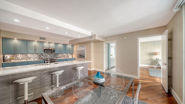 kitchen with tasteful backsplash, sink, hardwood / wood-style flooring, light stone counters, and a textured ceiling