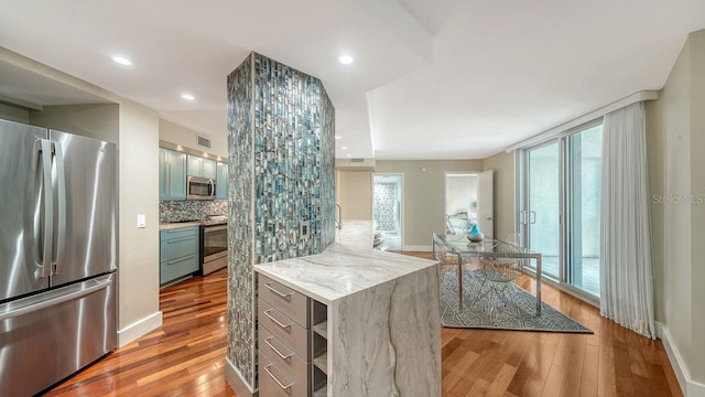 kitchen featuring stainless steel appliances, backsplash, light stone counters, and light hardwood / wood-style floors